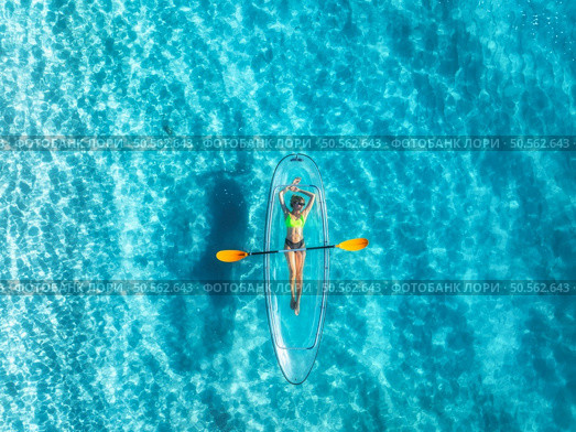 Aerial view of young woman lying on transparent canoe in blue sea at sunset. Summer in Zanzibar. Top drone view of beautiful slim girl, kanoe, ocean with clear water. Tropical background. Travel. Стоковое фото, агентство Ingram Publishing / Фотобанк Лори