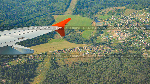 Airplane wing soaring over a picturesque landscape of green countryside, villages, and forests, offering a unique aerial perspective. Стоковое фото, фотограф Mikhail Davidovich / Фотобанк Лори