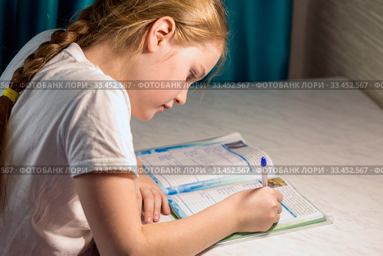 An adorable little schoolgirl sits at a desk and does homework in her room. Стоковое фото, фотограф Акиньшин Владимир / Фотобанк Лори