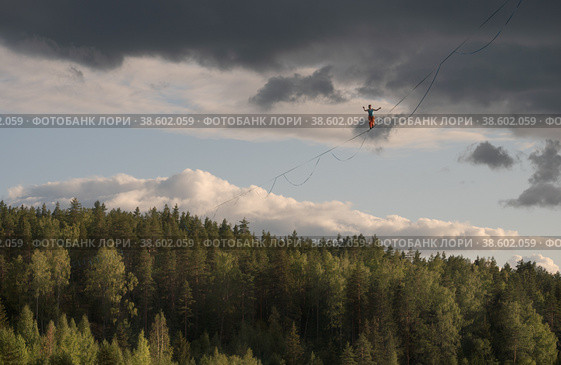 An extreme tightrope walker walks on a highline above the forest. Dramatic sky in background. Стоковое фото, фотограф Happyphotons / Фотобанк Лори