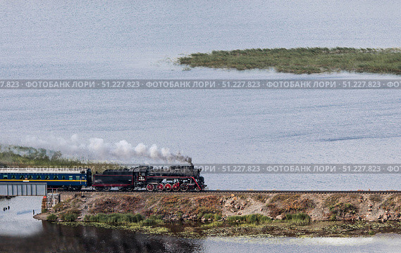 An old Soviet L-series steam locomotive. The Ruskeala Express retro train is driving along the lake. Side view from above. Russia, Republic of Karelia, Sortavala, August 11, 2025. Редакционное фото, фотограф Photojuli / Фотобанк Лори