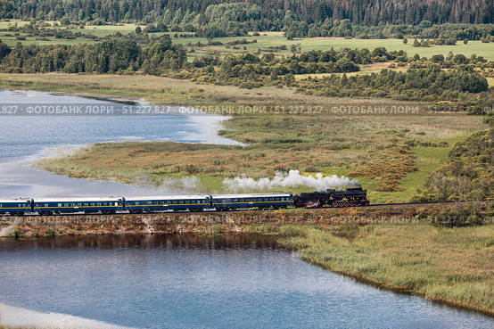 An old Soviet L-series steam locomotive. The Ruskeala Express retro train is driving along the lake. Side view from above. Russia, Republic of Karelia, Sortavala, August 11, 2025. Редакционное фото, фотограф Photojuli / Фотобанк Лори