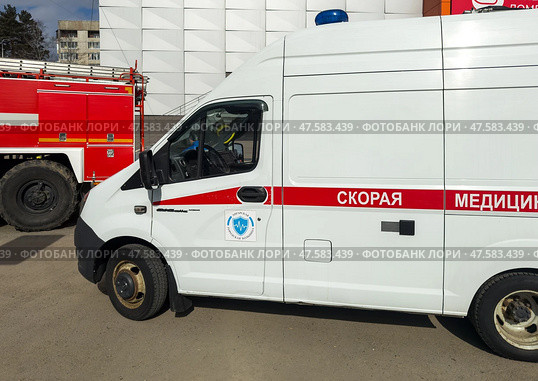 ANGARSK, IRKUTSK REGION, RUSSIA - April 08, 2025: Emergency vehicles on a city street. A red fire truck and a white ambulance near a crowded shopping mall Festival on sunny spring day. Редакционное фото, фотограф Виктория Катьянова / Фотобанк Лори