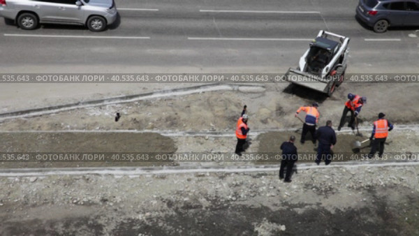 ANGARSK, IRKUTSK REGION, RUSSIA - May 23, 2023: Video of road workers in orange vests grading a walkway with a mini excavator. View from above. Редакционное видео, видеограф Виктория Катьянова / Фотобанк Лори