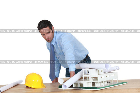 Annoyed architect piling rolled-up drawings on a model. Стоковое фото, агентство Ingram Publishing / Фотобанк Лори