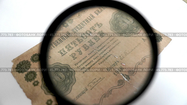 Антикварная банкнота 500 рублей 1918 года под увеличительным стеклом. Крупный план старинной купюры номиналом 500 рублей, выпущенной в 1918 году, рассматриваемой через увеличительное стекло. Видны декоративные узоры, номинал и текст с упоминанием обеспечения золотом. Также отображены подписи и серийный номер. Банкнота имеет заметные потертости и повреждения, что указывает на её возраст и историческую ценность. Стоковое фото, фотограф Анна Чижова / Фотобанк Лори