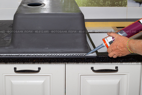 Applying black sanitary sealant with a nail gun to the edge of the kitchen sink. Installing a sink on a kitchen countertop. Стоковое фото, фотограф Коханова Наталья / Фотобанк Лори