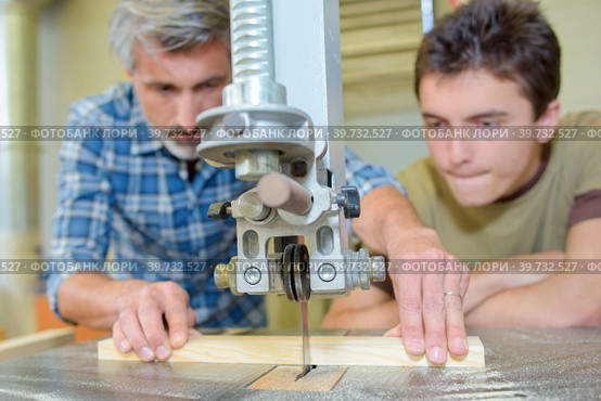 Apprentice carpenter watching how to use bench saw. Стоковое фото, фотограф Phovoi R. / Smarterpix / Фотобанк Лори