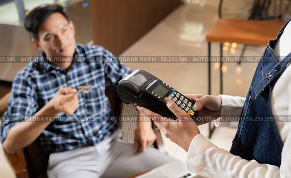 Asian customer using credit card with EMV chip technology to pay a waitress for coffee purchase at table in cafe. Стоковое фото, агентство Ingram Publishing / Фотобанк Лори
