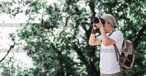 Asian traveler man with backpack taking a photo in the park with copy space. Travel photographer. Vocation and holiday concept. Стоковое фото, агентство Ingram Publishing / Фотобанк Лори