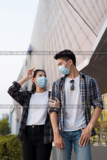 Asian Young Couple in protection mask standing outdoor of large building, They are discussion with happiness, New normal lifestyle amid coronavirus outbreak. Стоковое фото, агентство Ingram Publishing / Фотобанк Лори