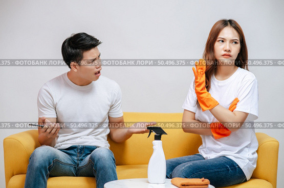 Asian young couple quarrels while cleaning in the living room, Young woman wearing gloves and holding spray bottle in hand with feel dissatisfied her husband, family issues and relationship concept. Стоковое фото, агентство Ingram Publishing / Фотобанк Лори