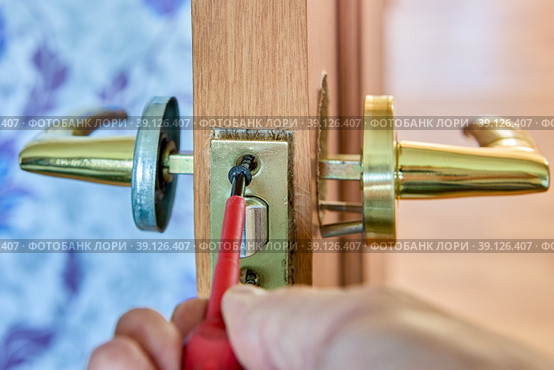 Assembling mechanism of lever door handle, locksmith tightens fixing screw using a screwdriver. Стоковое фото, фотограф Владимир Григорьев / Фотобанк Лори