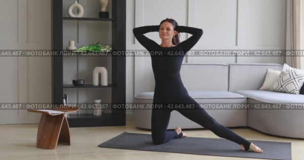 Athletic brunette performs side bends in parighasana, deadbolt pose, practicing yoga at home, training in black sports overalls on the mat, full-length view. Стоковое видео, видеограф Сергей Чайко / Фотобанк Лори