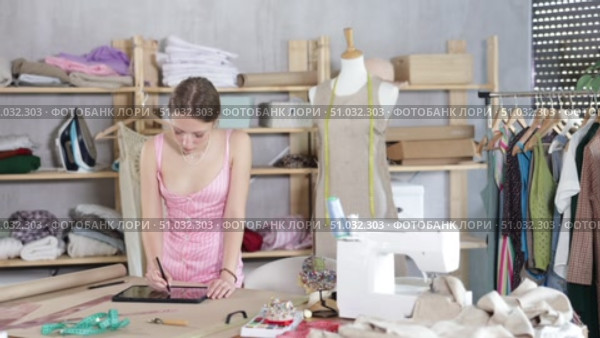 Attentive young female dressmaker drawing dress design in tablet in sewing workshop. Стоковое видео, видеограф Яков Филимонов / Фотобанк Лори