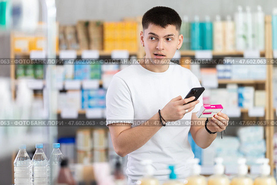 Attentive young guy client choosing box of paracetamol antipyretic pills, scan QR code on label, looking at composition of medicine in drug store. Стоковое фото, фотограф Яков Филимонов / Фотобанк Лори