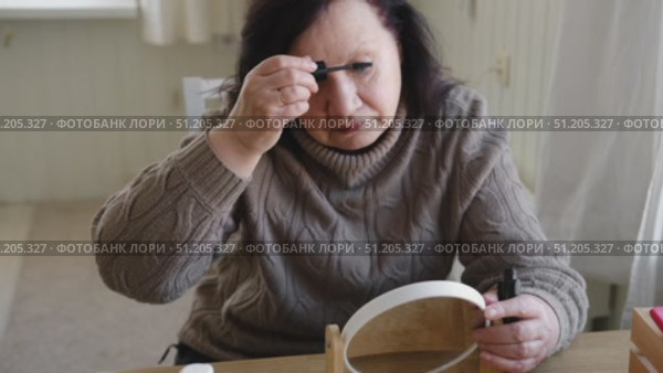 Attractive brunette senior woman putting on makeup looking in the mirror. Beautiful lady caring her face. Elderly female applied cosmetics. Natural old beauty and aging concept. Skin care and make-up. Стоковое видео, видеограф Марина Демидюк / Фотобанк Лори