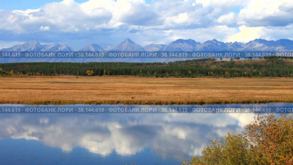 Autumn calm landscape with reflection in the river of a blue sky with clouds and a mountain range of the East Sayan. Natural autumnal background. Siberia, Buryatia, Tunka Valley. Стоковое видео, видеограф Виктория Катьянова / Фотобанк Лори