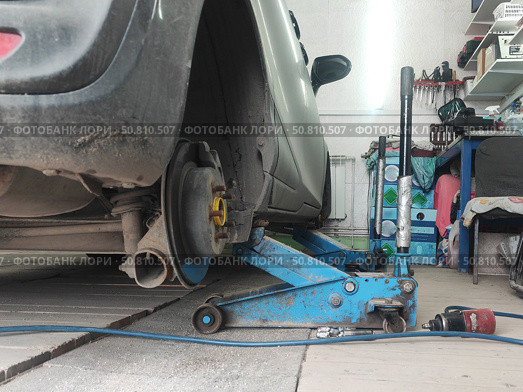 Автомобиль поднят домкратом, замена колеса в гараже. The car is filled with a jack, the wheel is replaced in the garage. Стоковое фото, фотограф Денис Баданин / Фотобанк Лори
