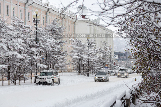 Автомобили едут по заснеженной улице северного города. После снегопада на проезжей части, тротуарах и деревьях лежит много снега. Магадан, Магаданская область, Сибирь, Россия. Стоковое фото, фотограф Андрей Степанов / Фотобанк Лори