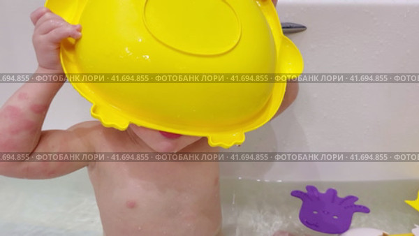 Baby drinks water from a ladle while sitting with toys in a white bathtub A happy child enjoys washing in the bathroom. Kid aged one year six months (18 months) Стоковое видео, видеограф Андрей Журавлев / Фотобанк Лори