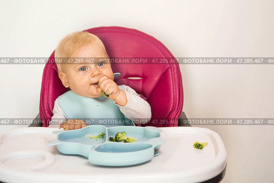 Baby food. The first meal. Feeding the baby. A cute little kid eats vegetables. Healthy food. The child is sitting on a high chair for feeding. Fresh vegetables and fruits. Стоковое фото, фотограф Photojuli / Фотобанк Лори