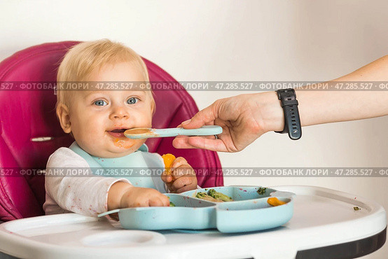 Baby food. The first meal. Feeding the baby. A cute little kid eats vegetables. Healthy food. The child is sitting on a high chair for feeding. Fresh vegetables and fruits. Стоковое фото, фотограф Photojuli / Фотобанк Лори