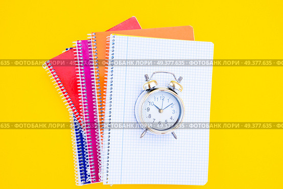 back to school concept - alarm clock on pile of notebooks, copy space on yellow background. back to school. Стоковое фото, агентство Ingram Publishing / Фотобанк Лори