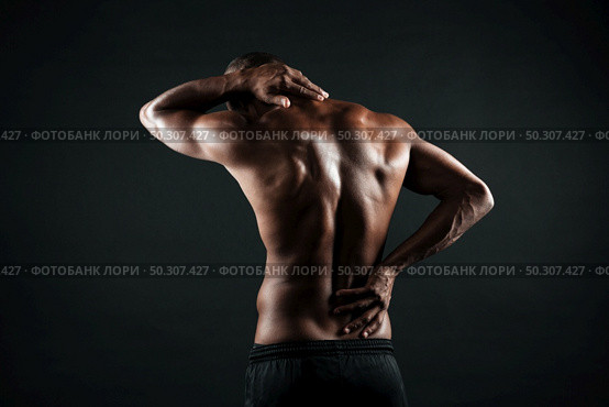Back view of young african sports man feeling pain in his back, isolated on black background. Стоковое фото, агентство Ingram Publishing / Фотобанк Лори