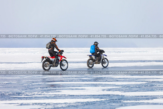 BAIKAL LAKE, IRKUTSK REGION, RUSSIA -  March 08, 2015: Two extreme tourists girls travels by motorcycles on ice of frozen Small Sea around Olkhon Island at cold winter day. Редакционное фото, фотограф Виктория Катьянова / Фотобанк Лори