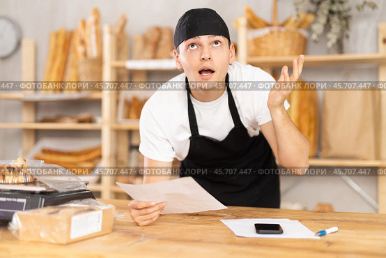 Bakery guy employee in apron examines documents, ponders debt restructuring. Стоковое фото, фотограф Яков Филимонов / Фотобанк Лори