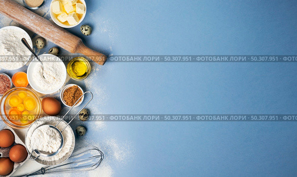 Baking ingredients for dough on blue background, top view of flour, eggs, butter, sugar and kitchen utensils for homemade baking with copy space for text. Baking ingredients on blue color background, top view. Стоковое фото, агентство Ingram Publishing / Фотобанк Лори