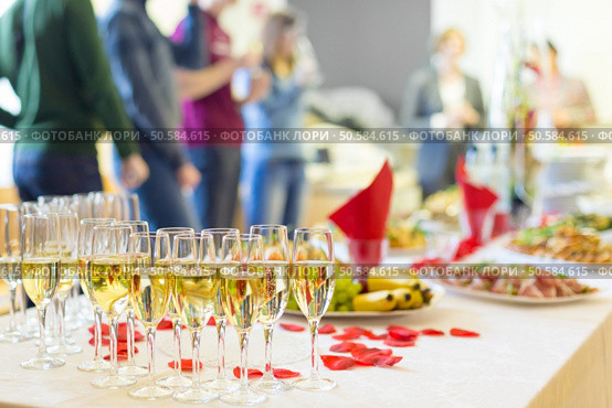 Banquet event. Table with the wineglasses, snacks and cocktails. People celebrating in the background.. Banquet event. Champagne on table. Стоковое фото, агентство Ingram Publishing / Фотобанк Лори