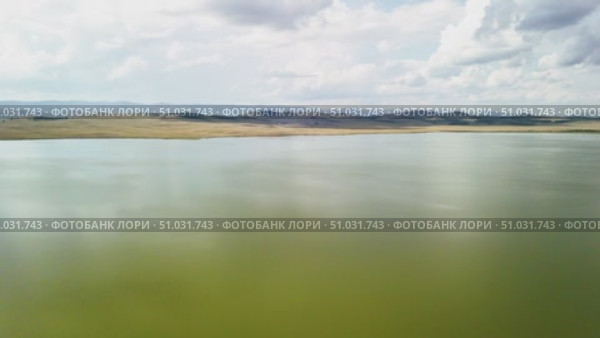 Bashkortostan, Russian Federation - August 07, 2025: Aerial view of tranquil lake reflecting clouds and mountains, showcasing serene landscape with lush greenery and open sky. Редакционное видео, видеограф Ирина Ручушкина / Фотобанк Лори