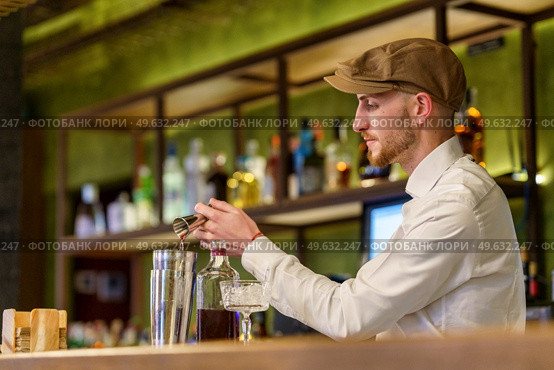 Bearded barman in white shirt and cap pouring liquor into shaker while preparing cocktail on counter in pub. Male barkeeper pouring alcohol into shaker. Стоковое фото, агентство Ingram Publishing / Фотобанк Лори