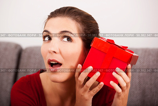 Beautiful and happy woman trying to guess what is inside the christmas present. Стоковое фото, агентство Ingram Publishing / Фотобанк Лори