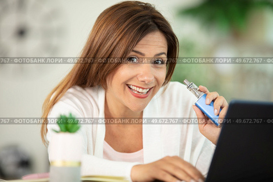 beautiful brunette smoke electronic cigarette and working on her laptop. Стоковое фото, агентство Ingram Publishing / Фотобанк Лори