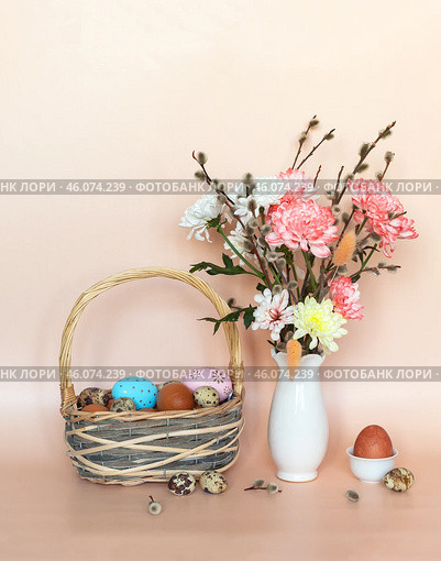 Beautiful Easter still life with spring bouquet of willow branches and chrysanthemum flowers and traditional painted Easter eggs in a wicker basket on a pink background. Empty space for text above. Стоковое фото, фотограф Виктория Катьянова / Фотобанк Лори