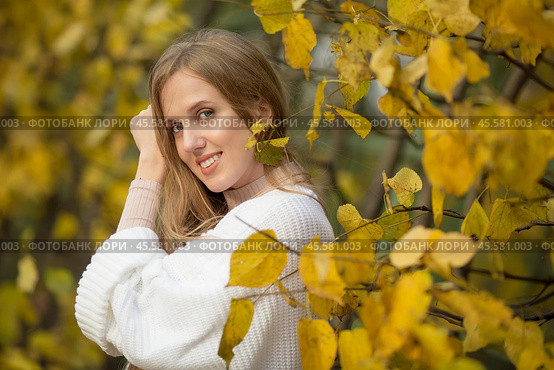 Beautiful happy girl with light brown hair among the yellow foliage in the autumn park. An attractive young woman is smiling and looking at the camera. Fall season. Leaves of golden color. Autumn mood. Стоковое фото, фотограф Андрей Степанов / Фотобанк Лори