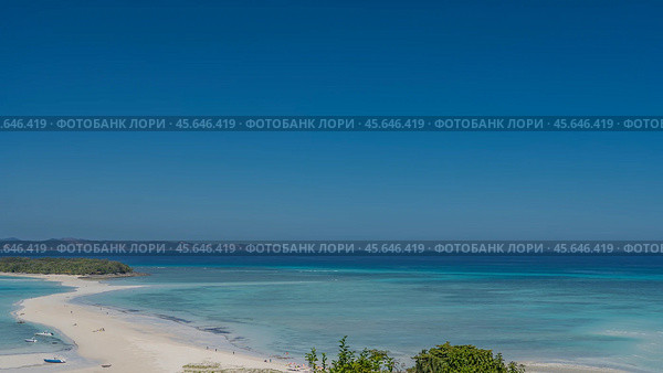 Beautiful postcard seascape. A sandbar winds through the aquamarine ocean to a small green island. Silhouettes of people on the beach. Boats on the water. Mountains on the horizon. Clear blue sky. Стоковое фото, фотограф Вера Ивановна Кубарева / Фотобанк Лори