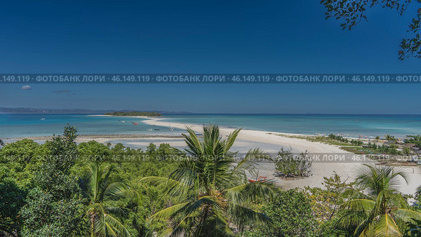Beautiful tropical postcard landscape. A winding sandbar in the aquamarine ocean. A green island in the distance. Boats at sea. Lush vegetation in the foreground. The blue sky. Madagascar. Nosy Iranja. Стоковое фото, фотограф Вера Ивановна Кубарева / Фотобанк Лори