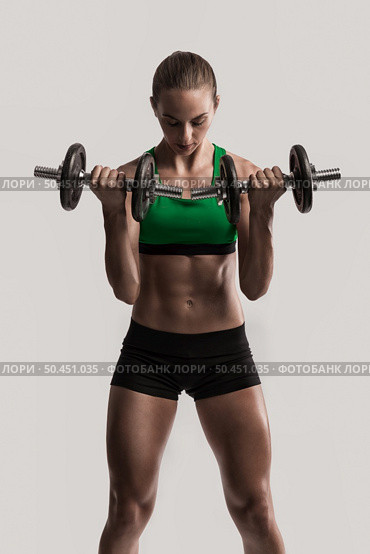 Beautiful young woman in a workout gear lifting dumbbells. Стоковое фото, агентство Ingram Publishing / Фотобанк Лори