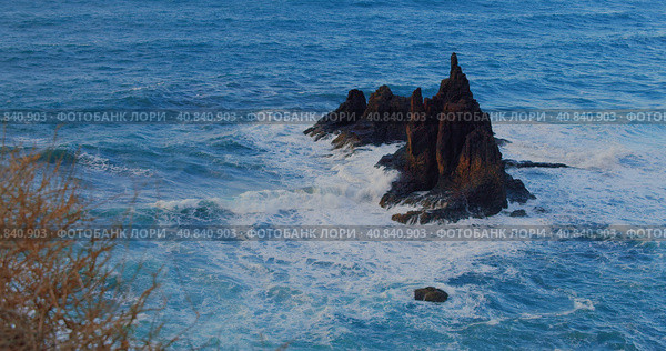 Big waves crash into the black volcanic rocks on the remote shore of Tenerife Island. Cinematic shot of a deep blue ocean swell violently splashing over the rocky coast of an exotic island. Стоковое фото, фотограф Ольга Сухарева / Фотобанк Лори