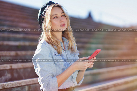 Blonde woman using her smartphone sitting on some city steps, wearing a denim shirt and black beret.. Blonde woman using a smartphone sitting on some city steps, wearing a denim shirt and black beret. Стоковое фото, агентство Ingram Publishing / Фотобанк Лори