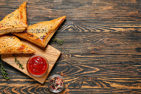 Board with tasty Uzbek samsa and tomato sauce on wooden background. Стоковое фото, фотограф Pixel_shot / Фотобанк Лори
