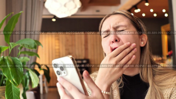 Bored young woman holds mobile phone iPhone, yawning. People lifestyle concept. Did not get enough sleep last night after party and barely got up in the morning. Стоковое видео, видеограф Сахарова Мария Юрьевна / Фотобанк Лори