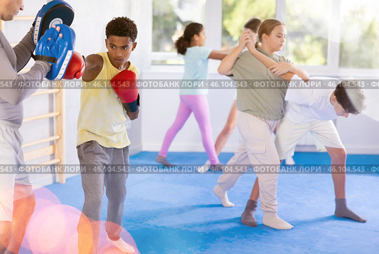 Boy hitting the focus mitts held by his boxing trainer in gym. Стоковое фото, фотограф Яков Филимонов / Фотобанк Лори