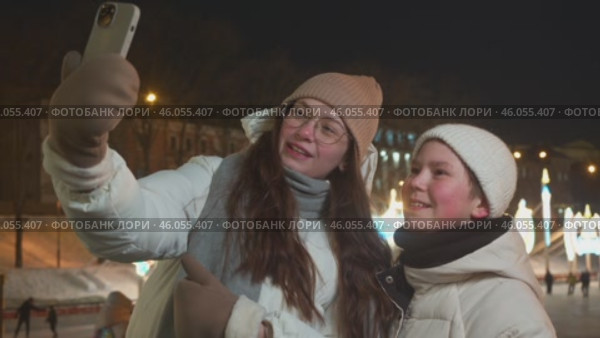 Boy takes photo with his mom in front of big ice rink with lights and decorations. boy and mom wave to people on internet. They smile and look happy. Стоковое видео, видеограф Strunov David / Фотобанк Лори