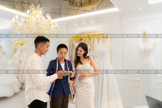 Bridal gown designers and tailors measure the size of the gown against the bride’s figure when she comes to try on the gown in order to make it perfect and ready to wear on the wedding day. Стоковое фото, агентство Ingram Publishing / Фотобанк Лори