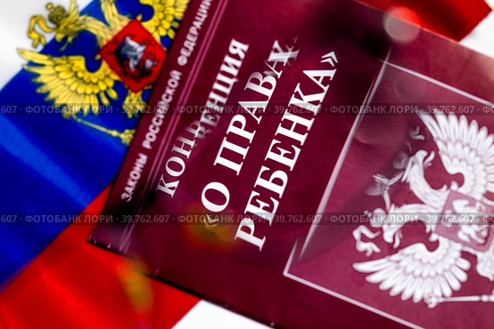 Брошюра с конвенцией "О правах ребенка" на фоне флага Российской Федерации лежит на столе (2023 год). Редакционное фото, фотограф Николай Винокуров / Фотобанк Лори